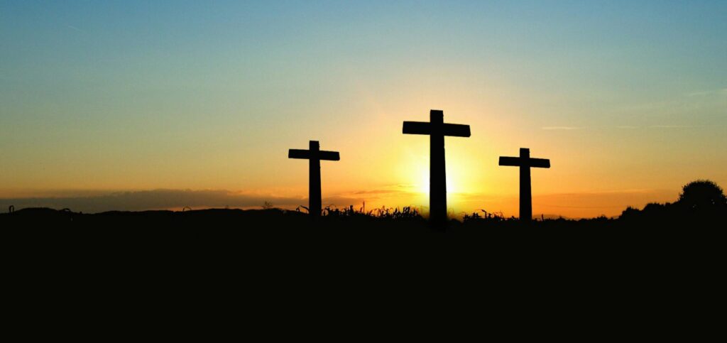 Silhouette of three crosses against a vibrant sunset sky.
