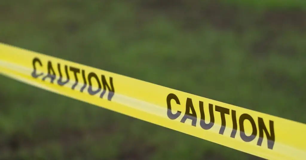 Close-up image of yellow caution tape in a grassy outdoor setting, symbolizing safety and warning.