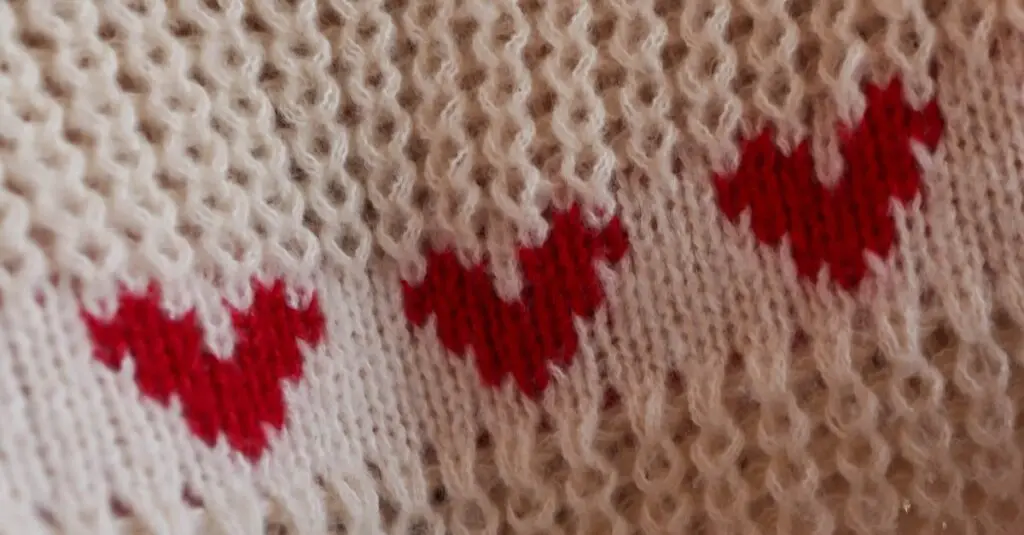 Close-up of a knitted fabric featuring red heart patterns on a soft beige background.