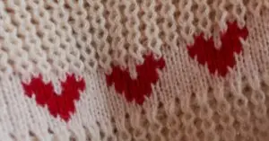 News Close-up of a knitted fabric featuring red heart patterns on a soft beige background.
